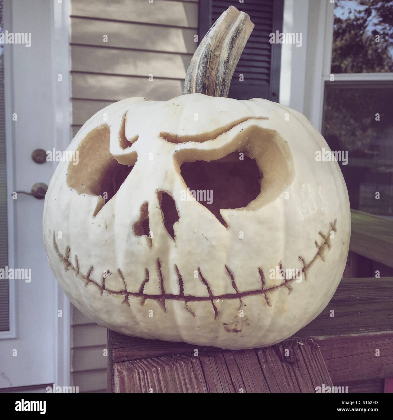 White pumpkin with a creepy face carved into it sits on the porch