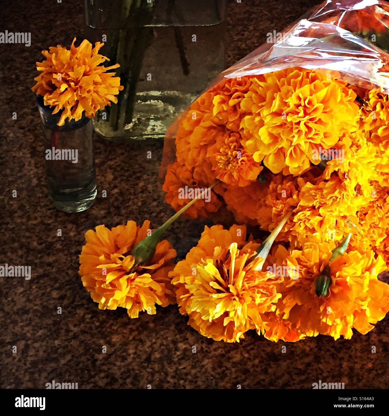 A single marigold flower is in a little vase next to a whole bouquet of