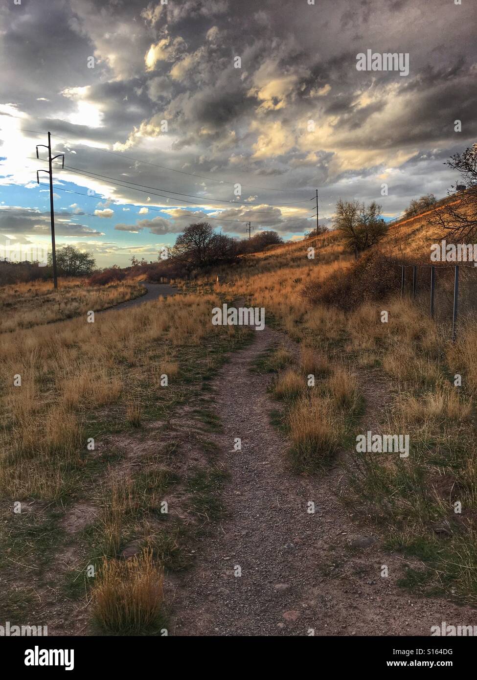 A dirt path winds along next to a paved bike trail on an autumn afternoon. Stock Photo