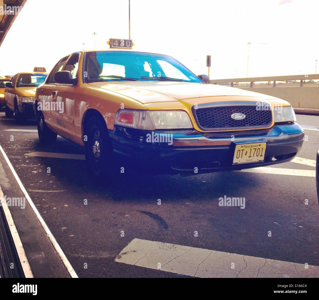 Ford Crown Victoria yellow taxi cab and JFK airport in New York. For years the Crown Vic has been the US's taxi of choice, often ex-police cars, but is being phased out in favour of hybrids - Smartphone Captured Stock Image