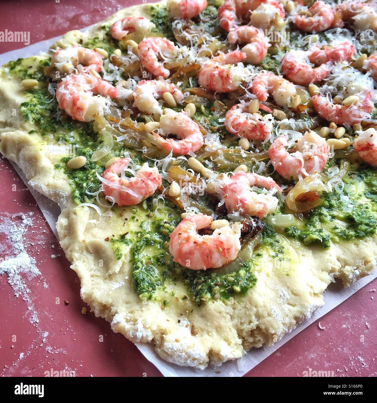 Homemade pizza crust topped with pesto, freshly caught prawns, pine nuts and cheese is ready for the oven. Stock Photo