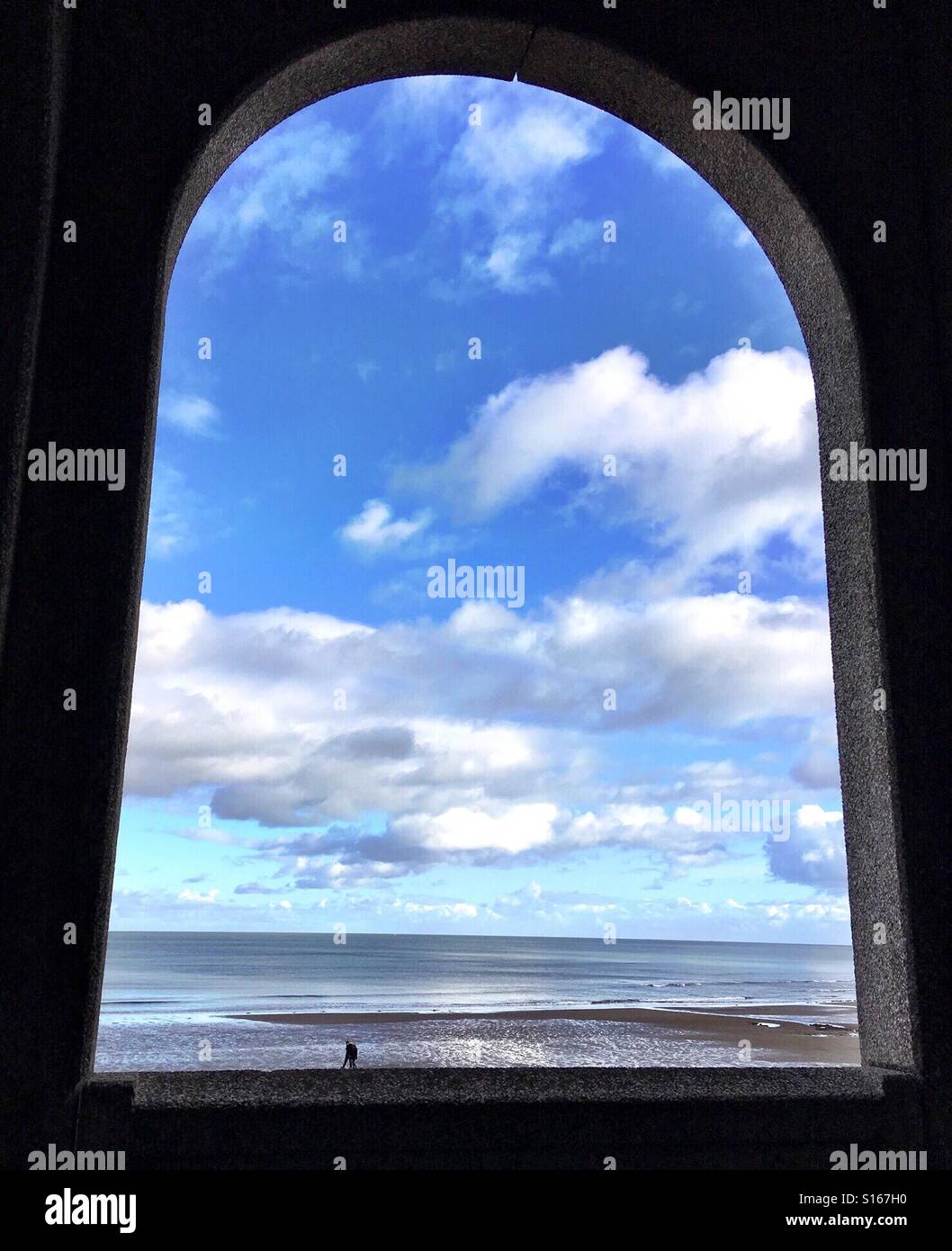 Couple walking on a beach with big sky, seen through an arch - Smartphone Captured Stock Image