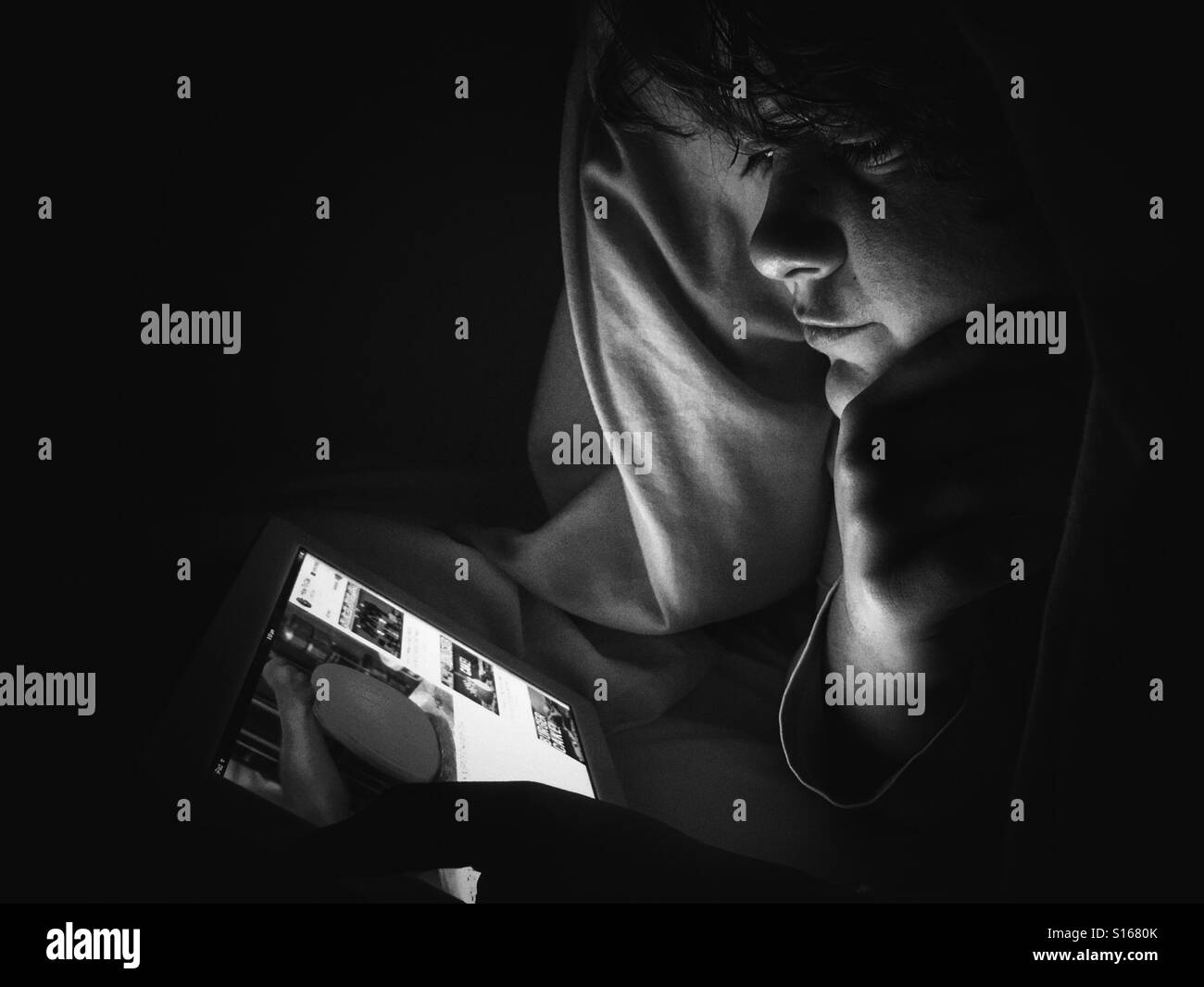 Teenager using an iPad at night, under duvet - Smartphone Captured Stock Image