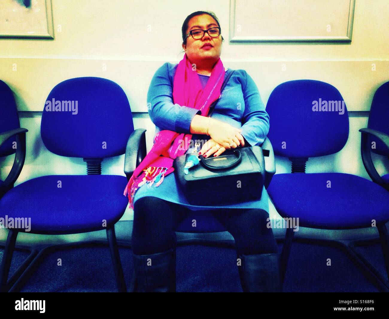 A woman sits and waits in a waiting room. - Smartphone Captured Stock Image