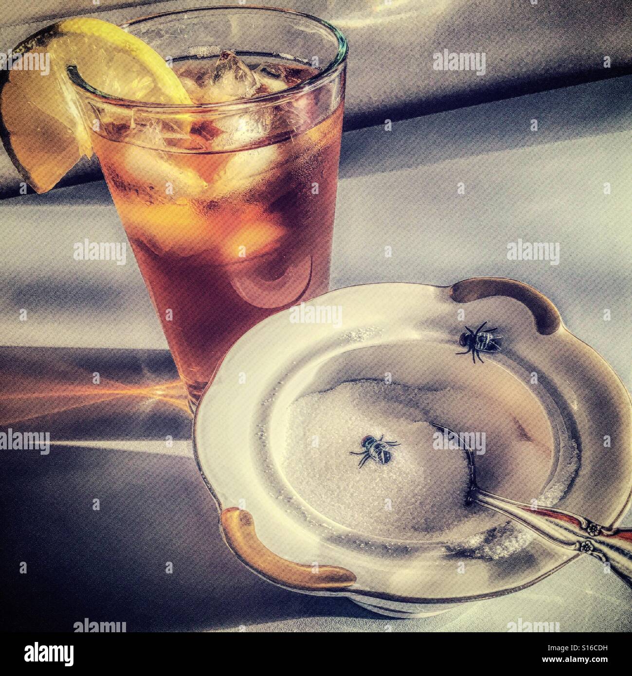 Sugar bowl with houseflies next to a glass of iced tea. Stock Photo