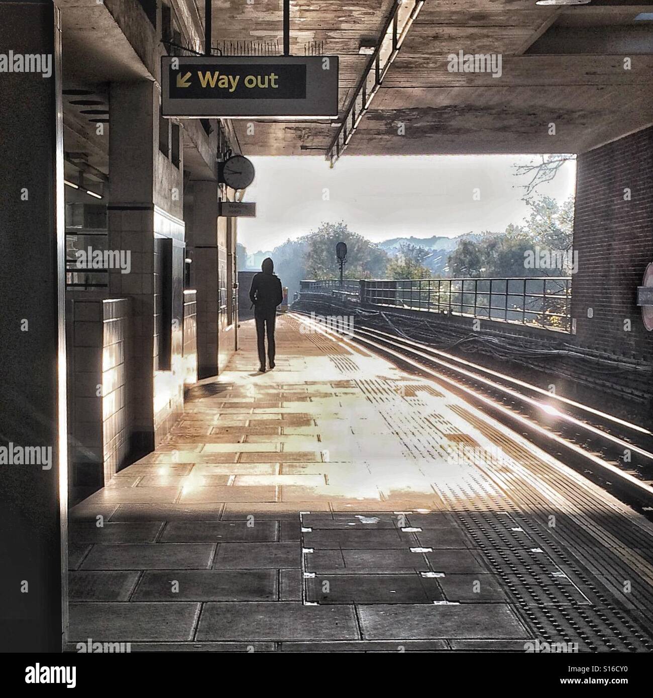 Lone figure on railway platform, beneath a Way Out sign. Stock Photo