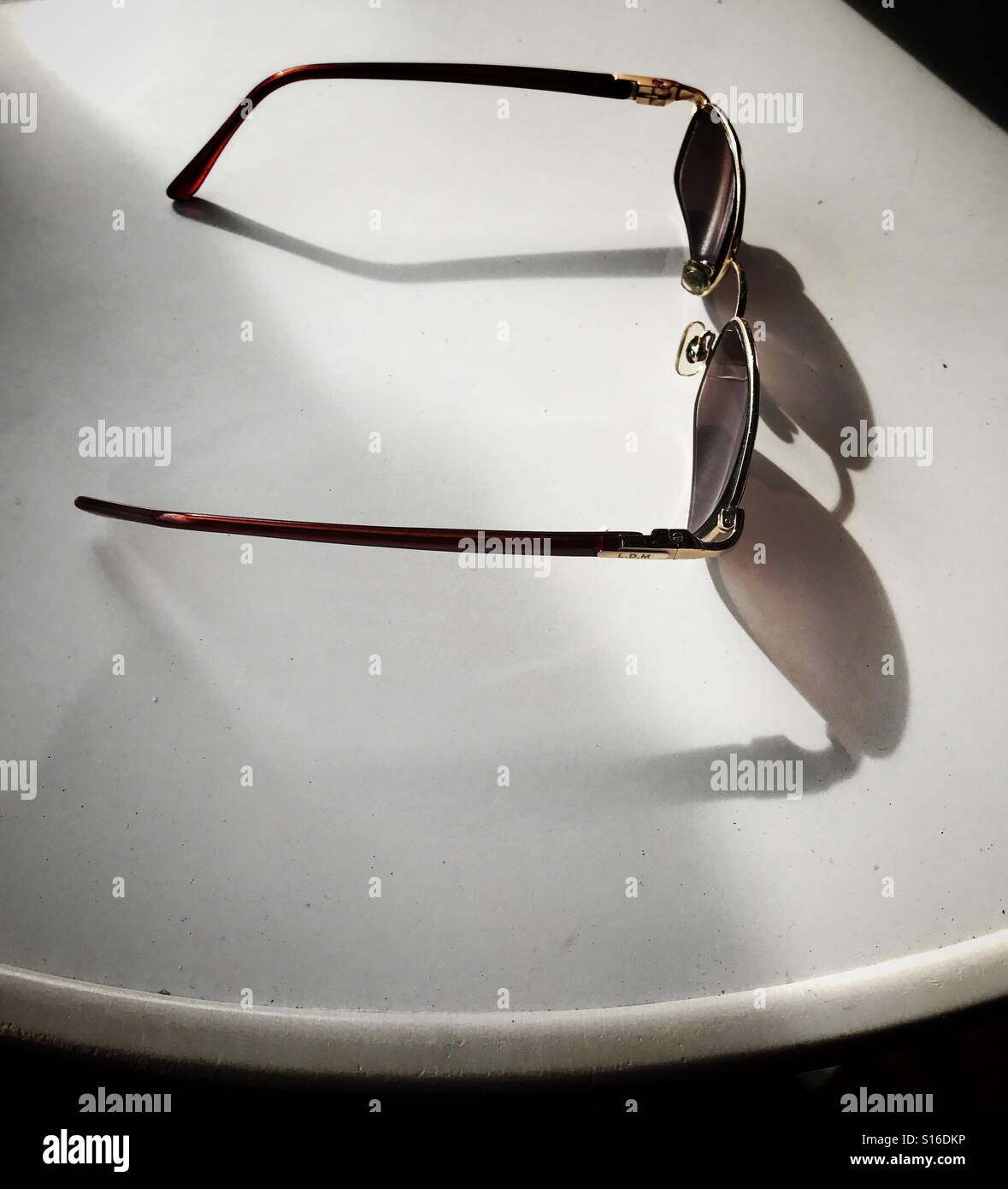 A pair of dark spectacles on a white table casting a shadow - Smartphone Captured Stock Image