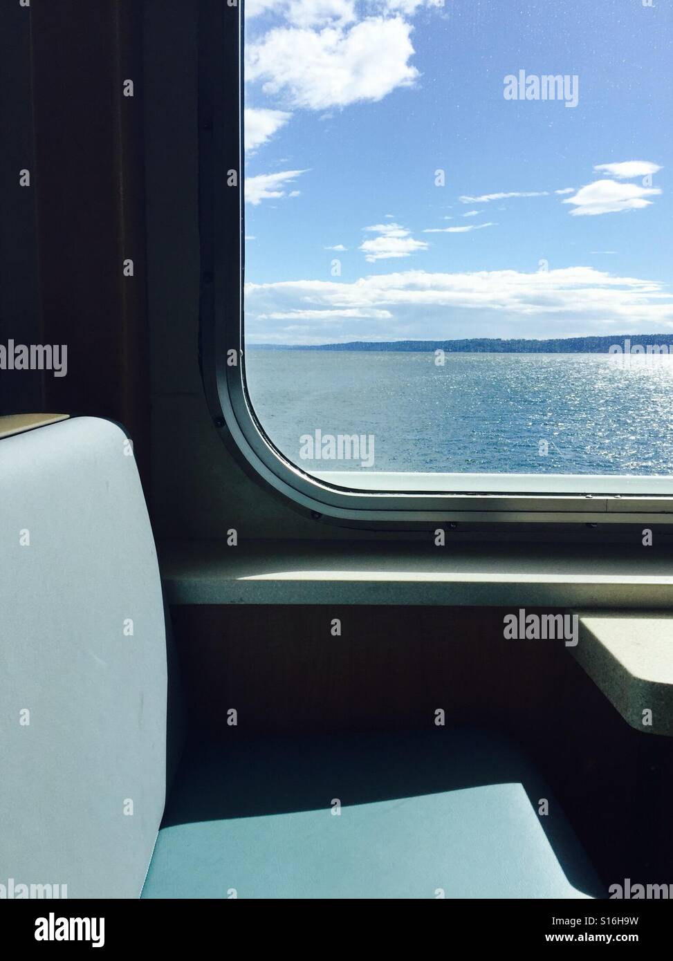 Looking out a ferry window showing the water and an island in the distance with a blue sky and clouds - Smartphone Captured Stock Image