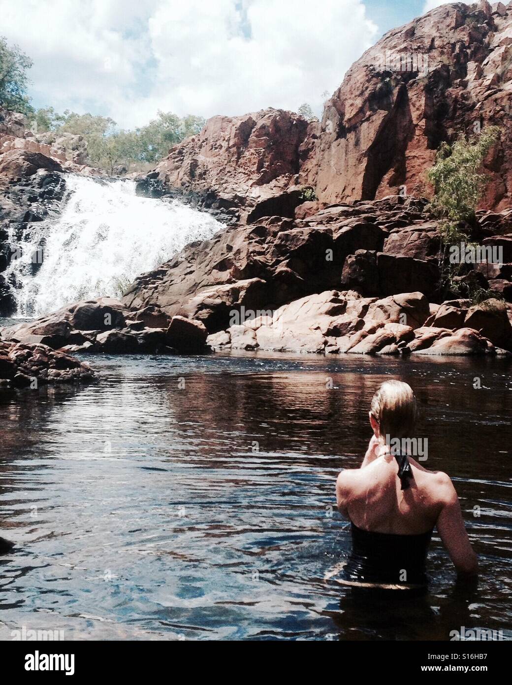 Woman swimming in water hole looking at waterfall Stock Photo