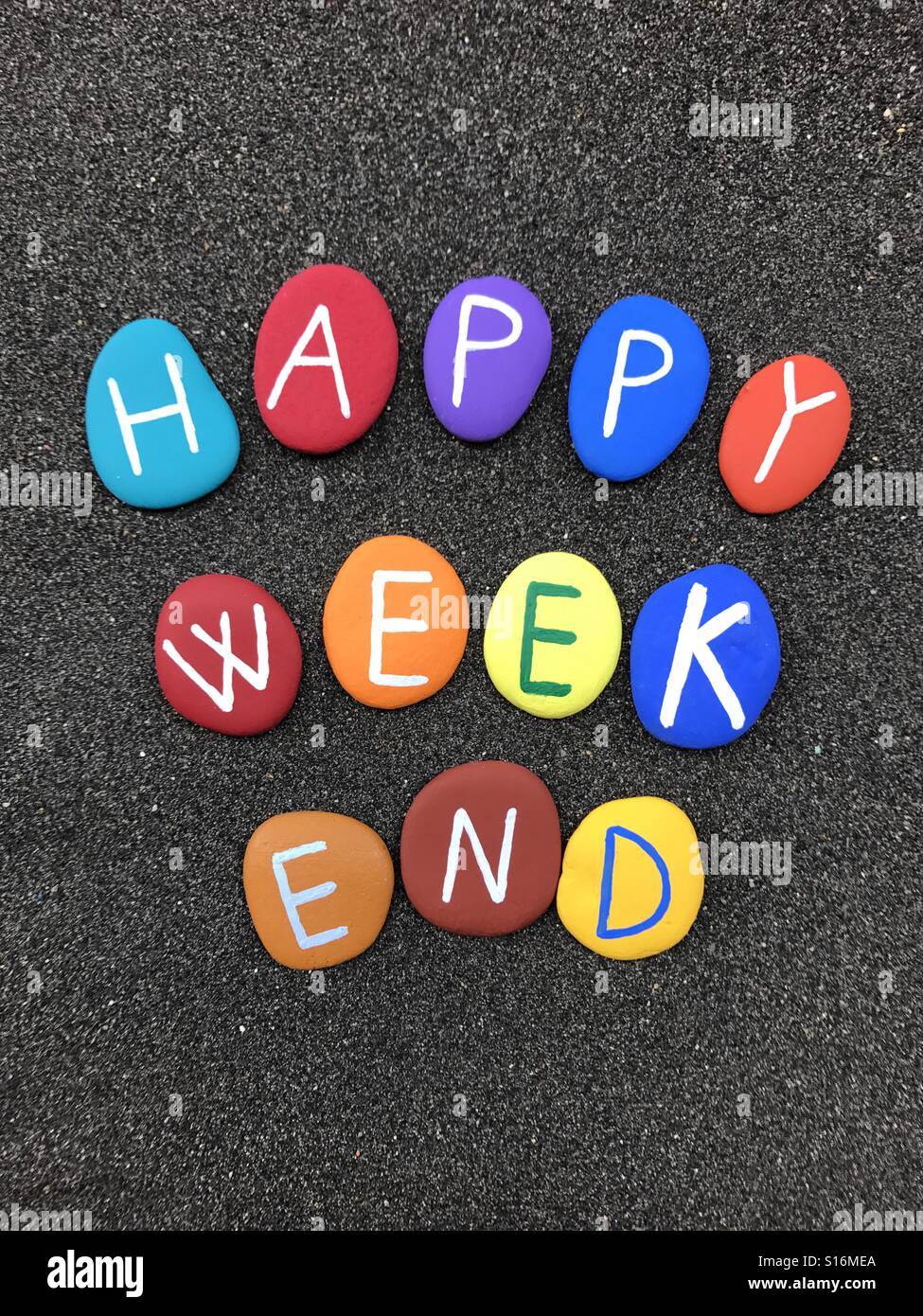 Happy weekend message composed with hand painted multi colored stone letters over volcanic sand - Smartphone Captured Stock Image