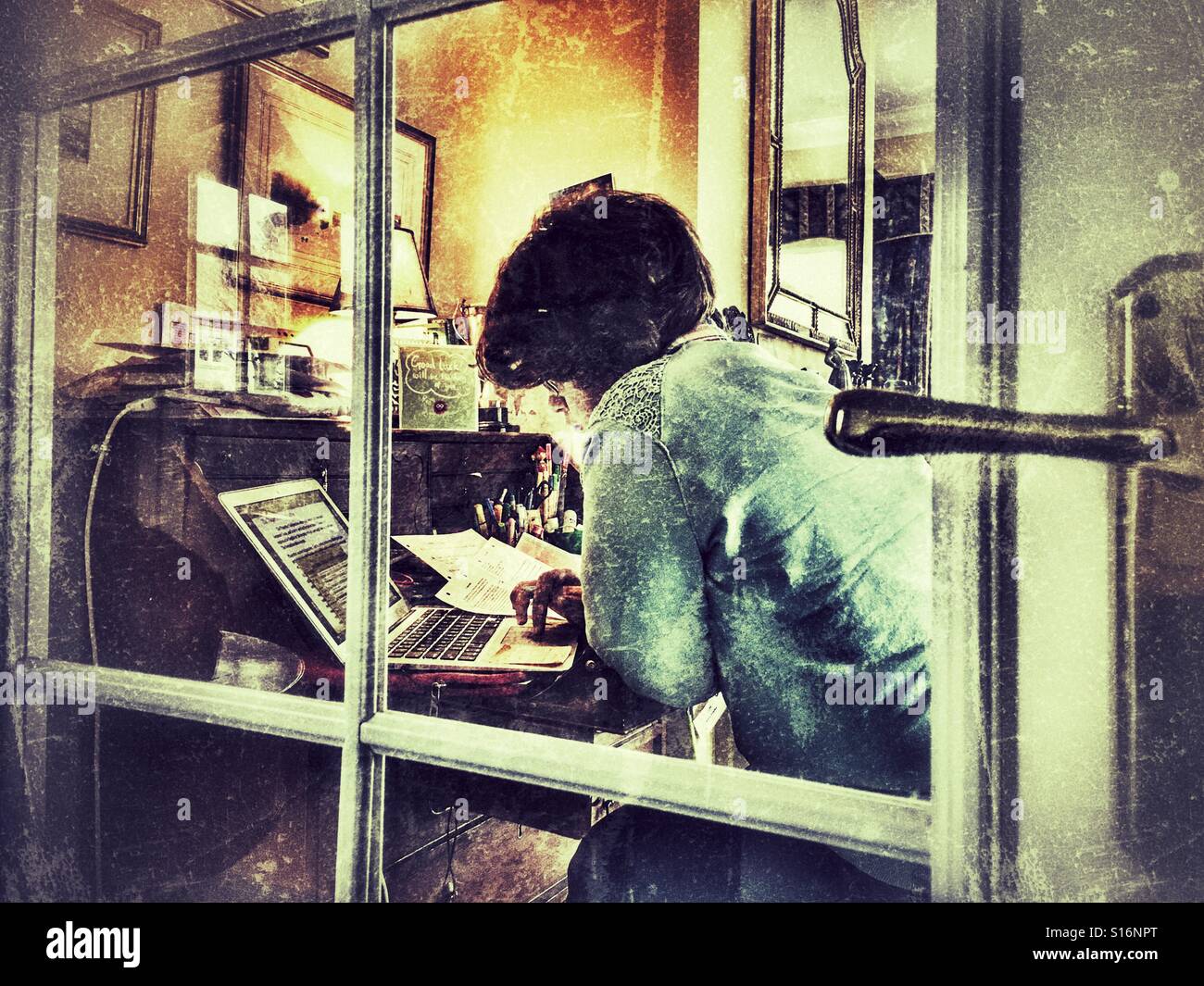 Student at her desk, using laptop computer. Seen through a glass door. - Smartphone Captured Stock Image
