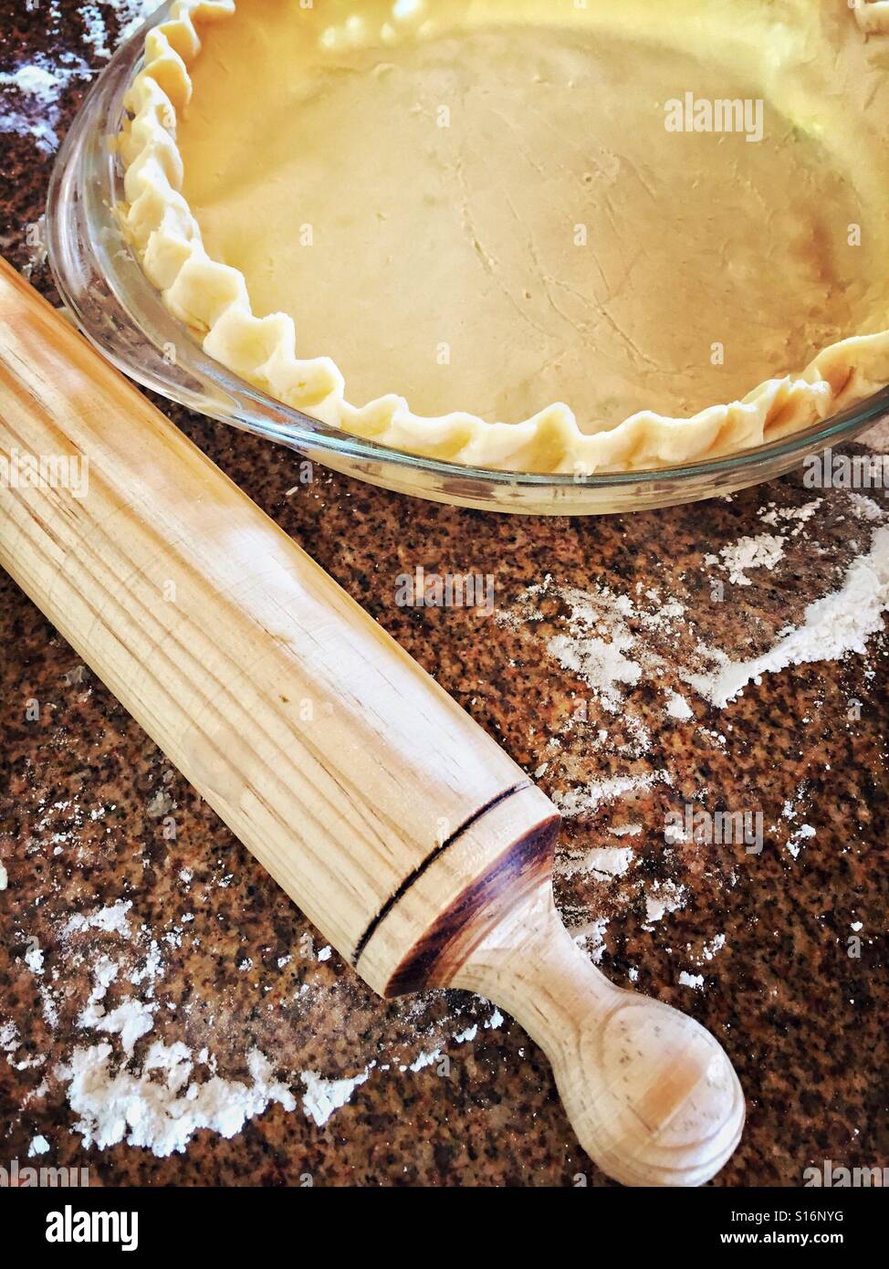 Raw pie dough has been rolled out with a rolling pin and placed inside a pie plate ready to fill and bake. Stock Photo