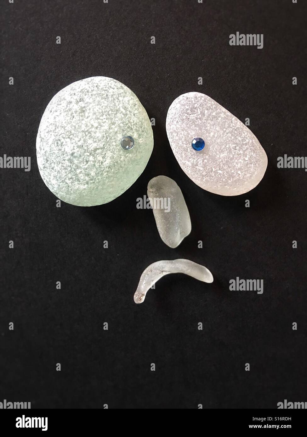 4 pieces of sea glass forming a face expressing dismay, on a black background Stock Photo