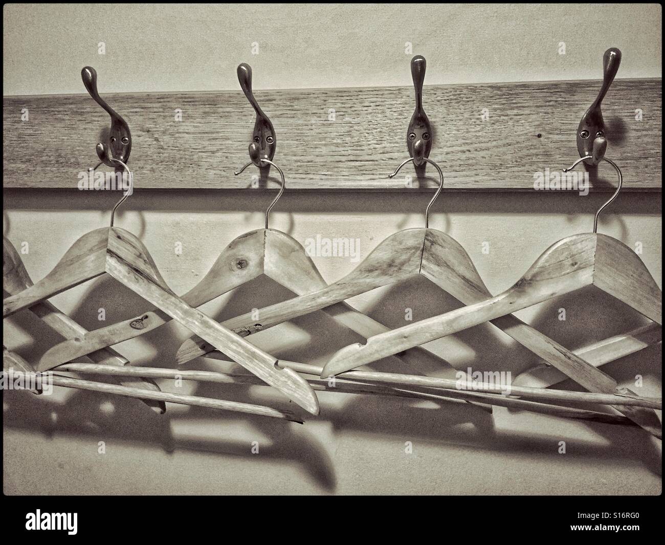 A toned monochrome image of wooden coat hangers lined up and waiting to