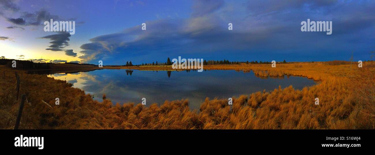 Small lake at sunset showing evergreens and reflections on far shore - Smartphone Captured Stock Image