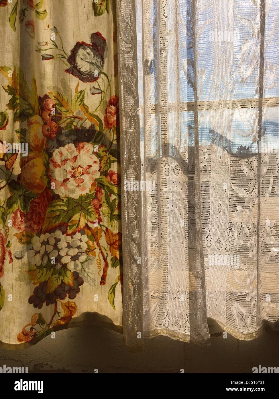 Vintage curtains brushed against a lace sheer covering a window at sundown. Stock Photo