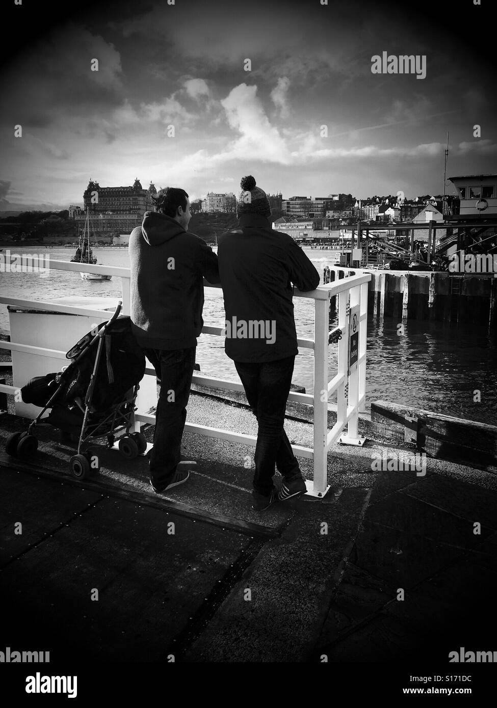 Couple leaning on a rail and watching the activities around a harbour - Smartphone Captured Stock Image