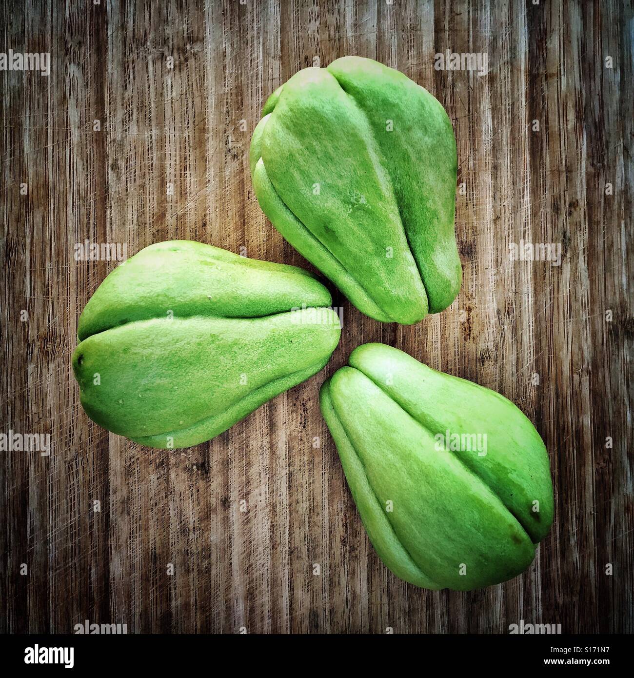 Three whole chayote fruit, also known as cho-cho or pear squash, are placed on a cutting board. Stock Photo