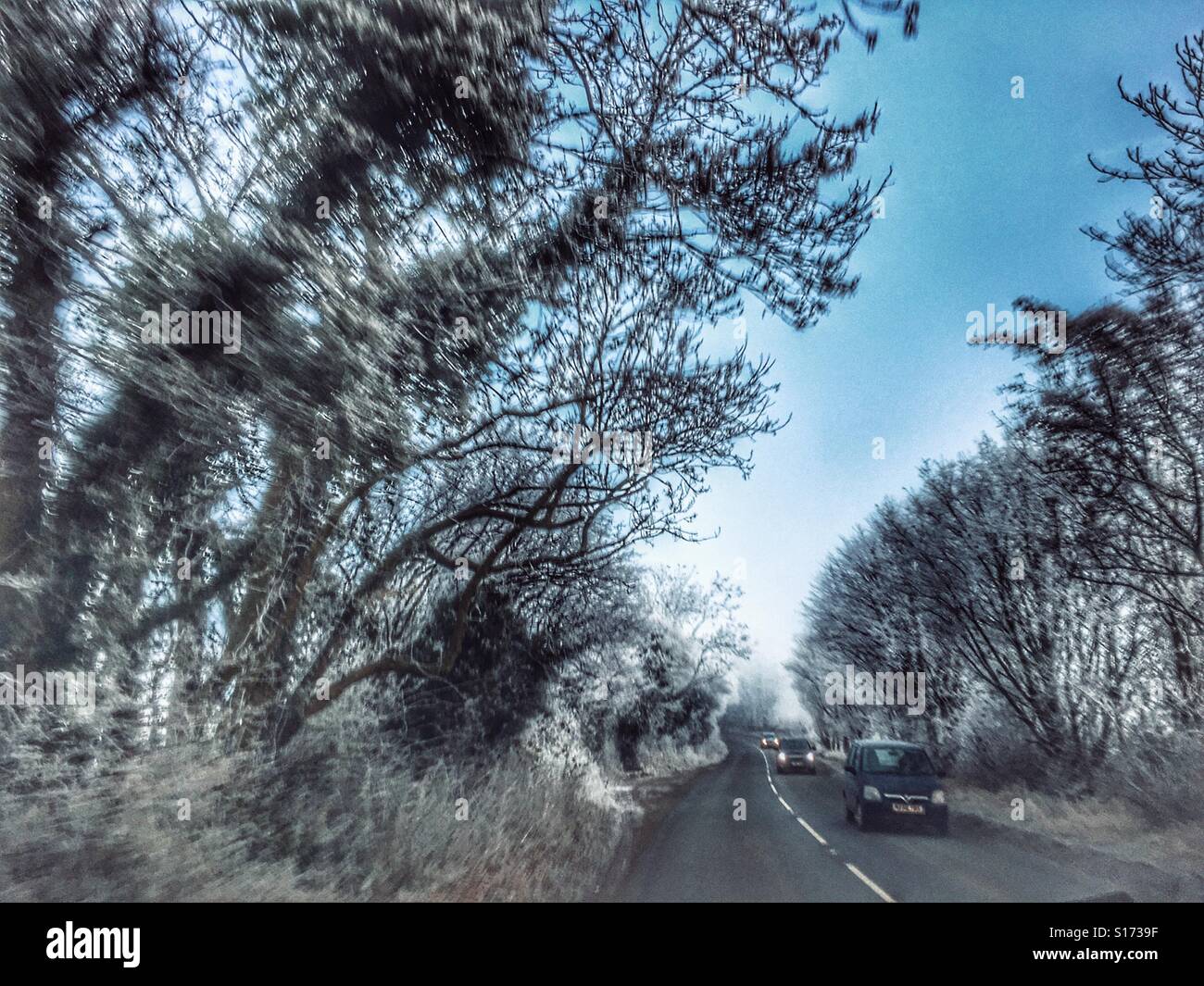 Driver's view through the front windscreen to the road ahead in winter. Heavy hoar frost, icy conditions and cars approaching with headlights. Early morning. - Smartphone Captured Stock Image