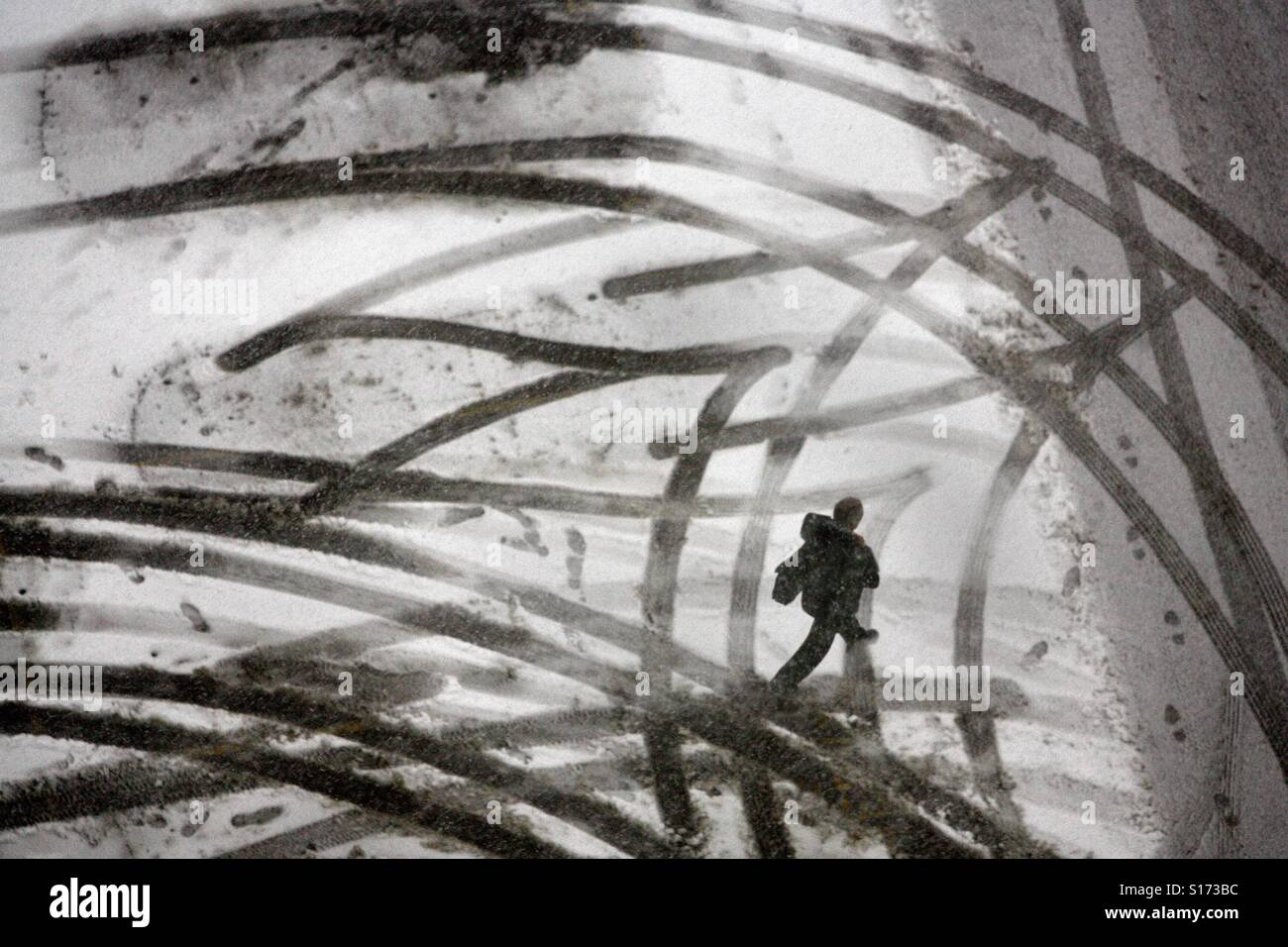 A pedestrian walks across a snow covered parking lot covered with tire tracks - Smartphone Captured Stock Image