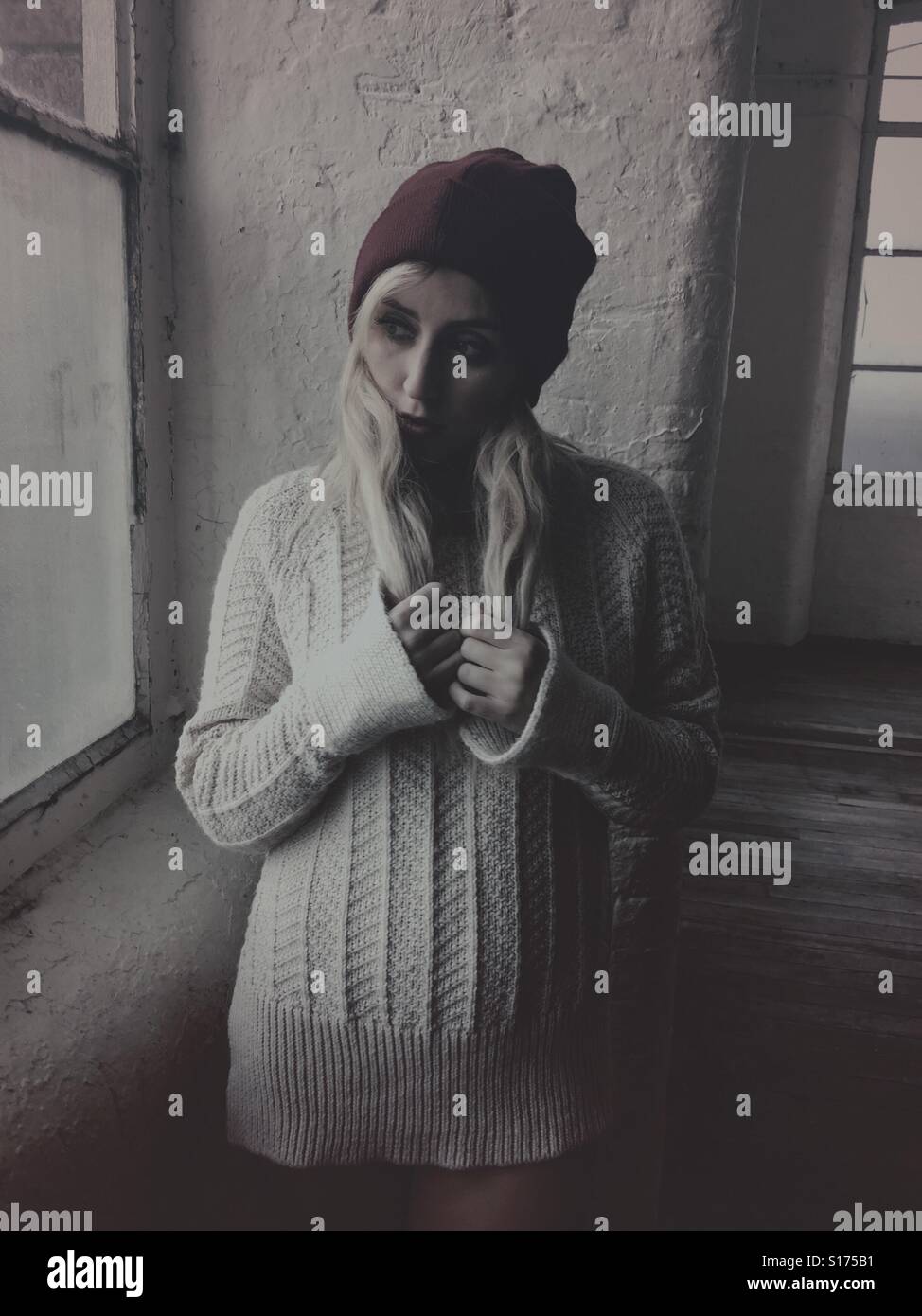 Thoughtful young woman wearing a wool jumper and hat standing by the window - Smartphone Captured Stock Image