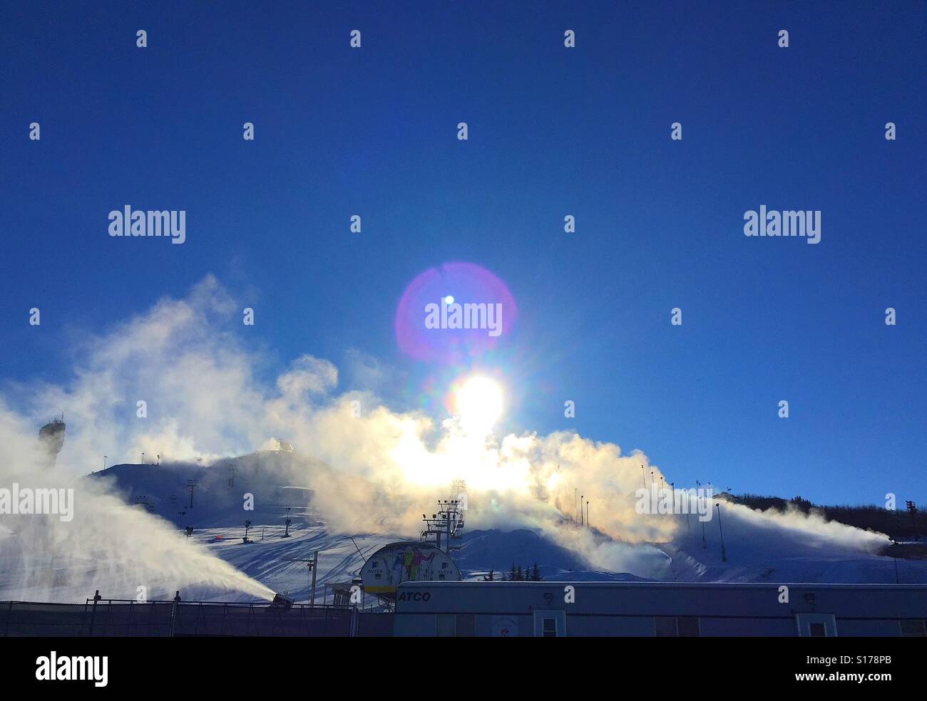 Preparing the ski hill - making snow with bright sun and lens flare in the background Stock Photo