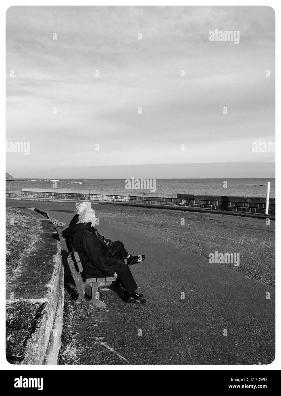 Black and white image of older couple sitting on a bench looking at the sea Stock Photo