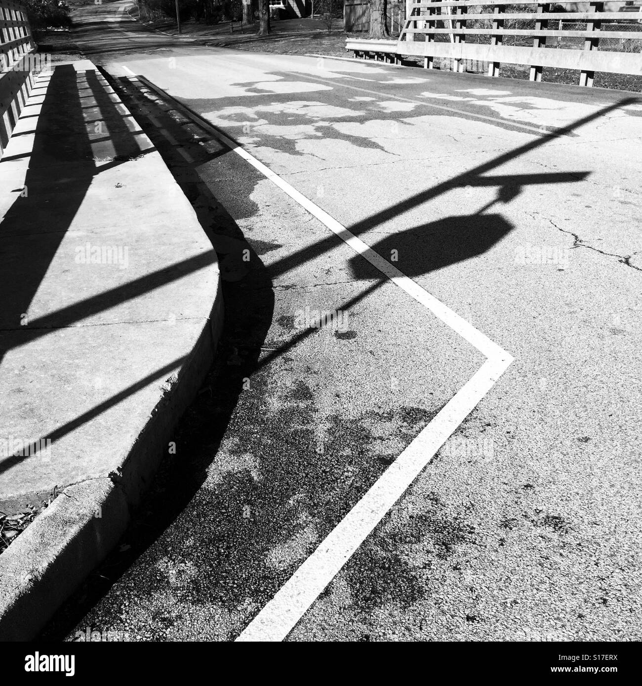 Shadow of stop sign, street sign and bridge railings with street markings at intersection of road and bridge at Noon, December. - Smartphone Captured Stock Image