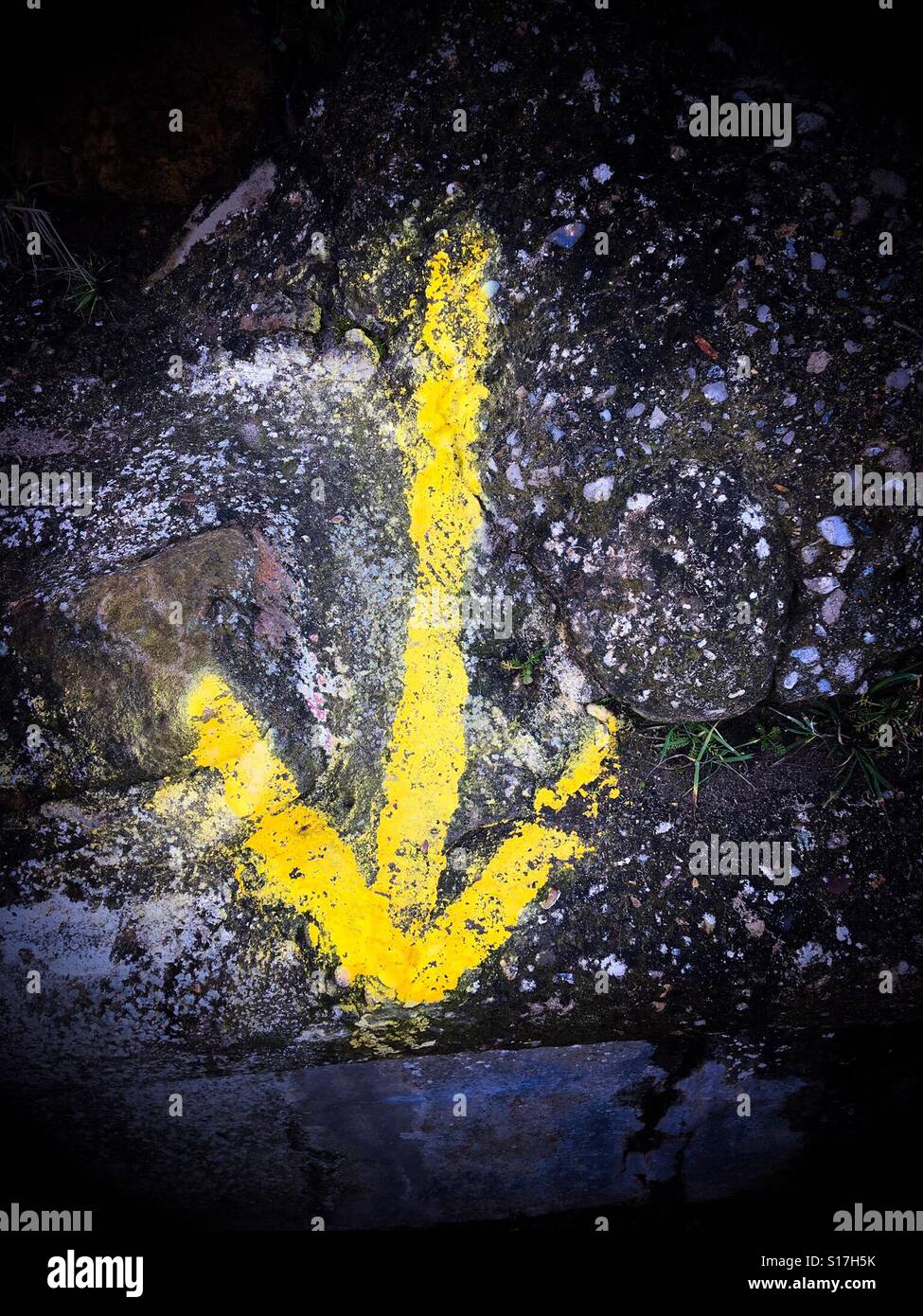 Spray painted yellow arrow on a stone wall pointing downward - Smartphone Captured Stock Image