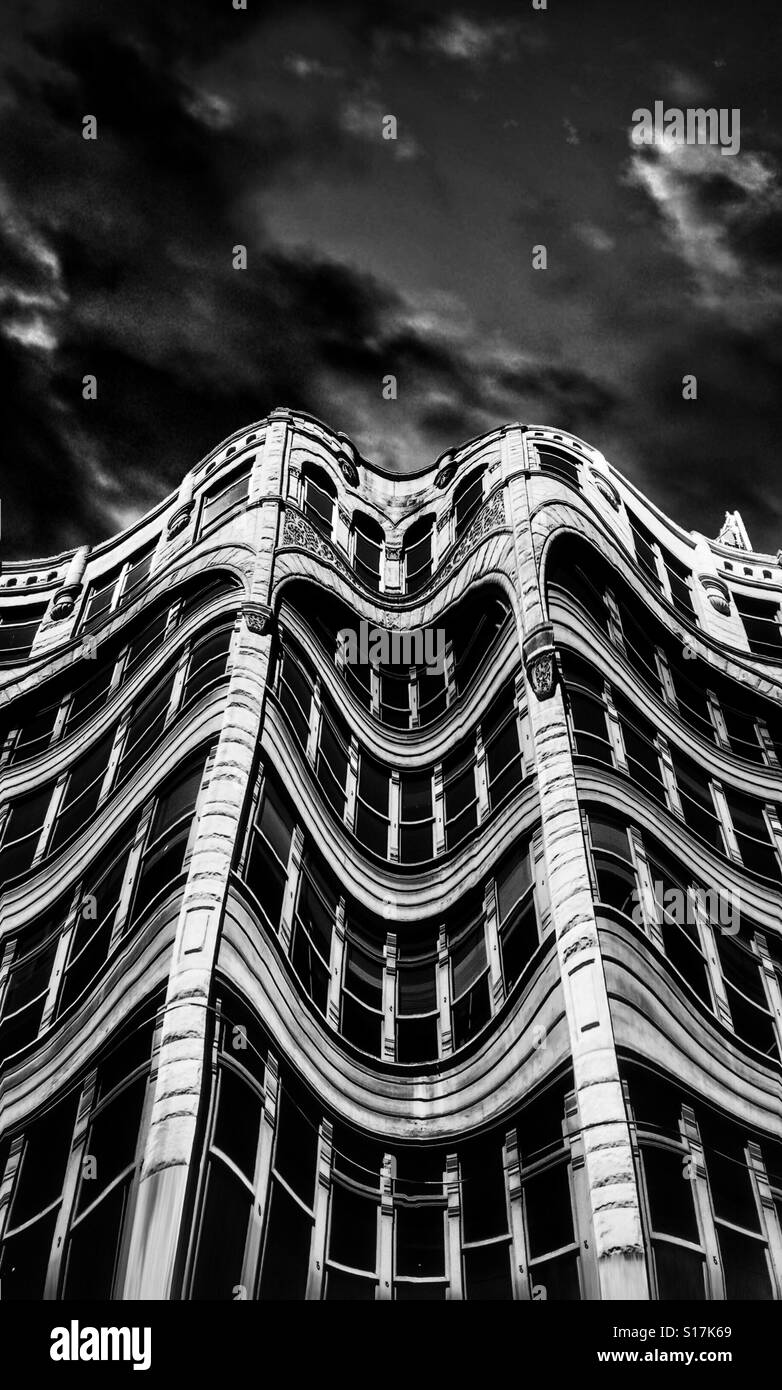 An abstract black and white image of a distorted building with many windows against a dark stormy sky - Smartphone Captured Stock Image