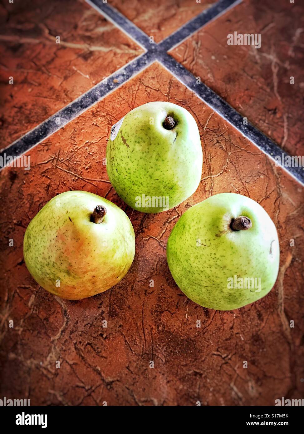 Three ripe pears are on a tile countertop. Stock Photo