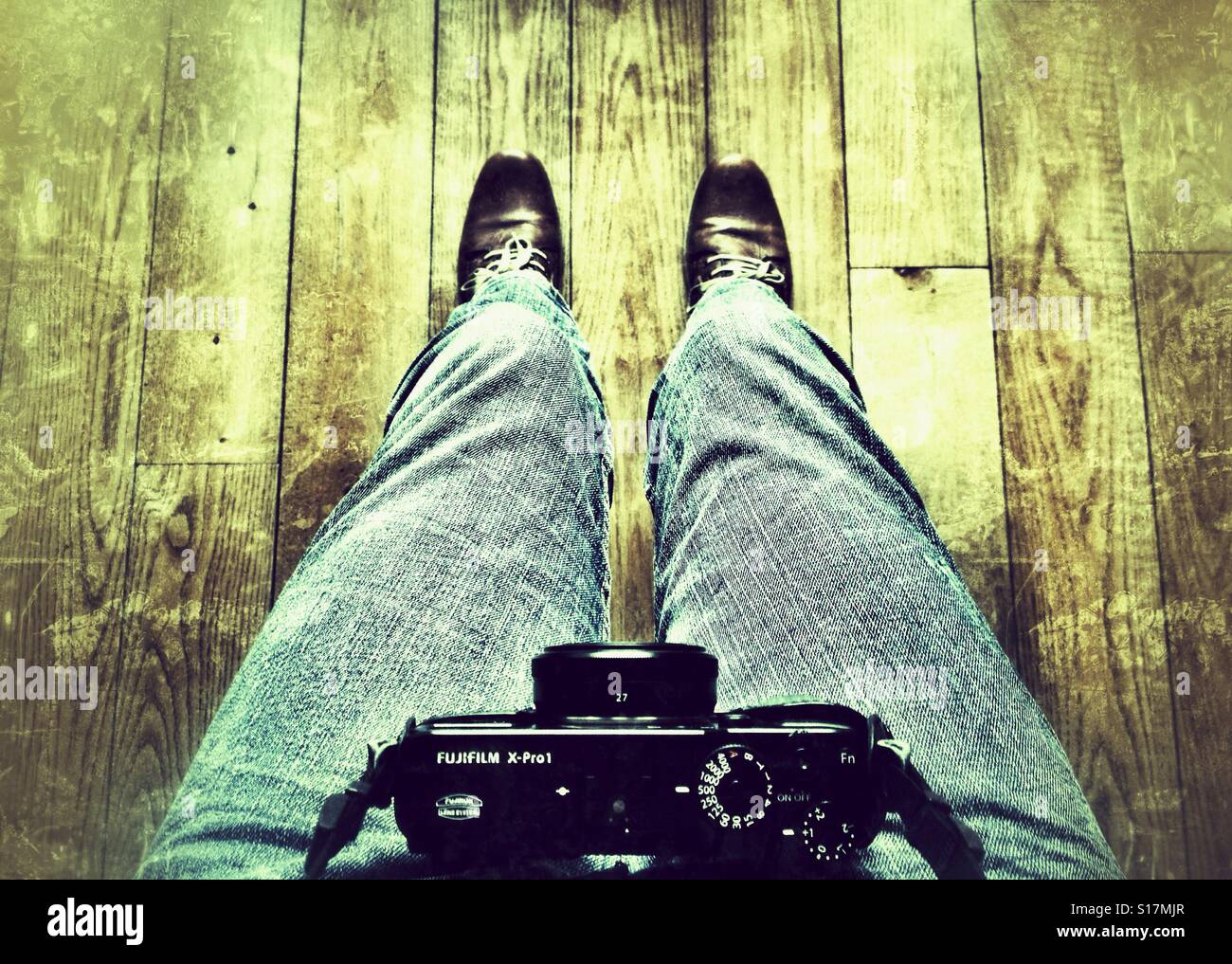 Man is standing on a wooden floor holding a mirrorless  camera on his belly grunge pattern - Smartphone Captured Stock Image