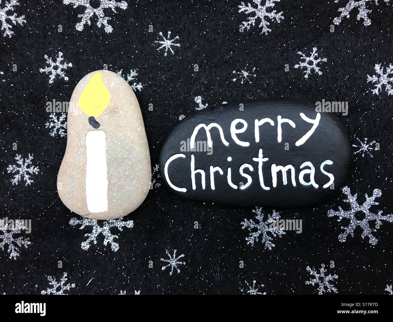 Merry Christmas text hand carved on a black painted stone with a carved stone candle design - Smartphone Captured Stock Image