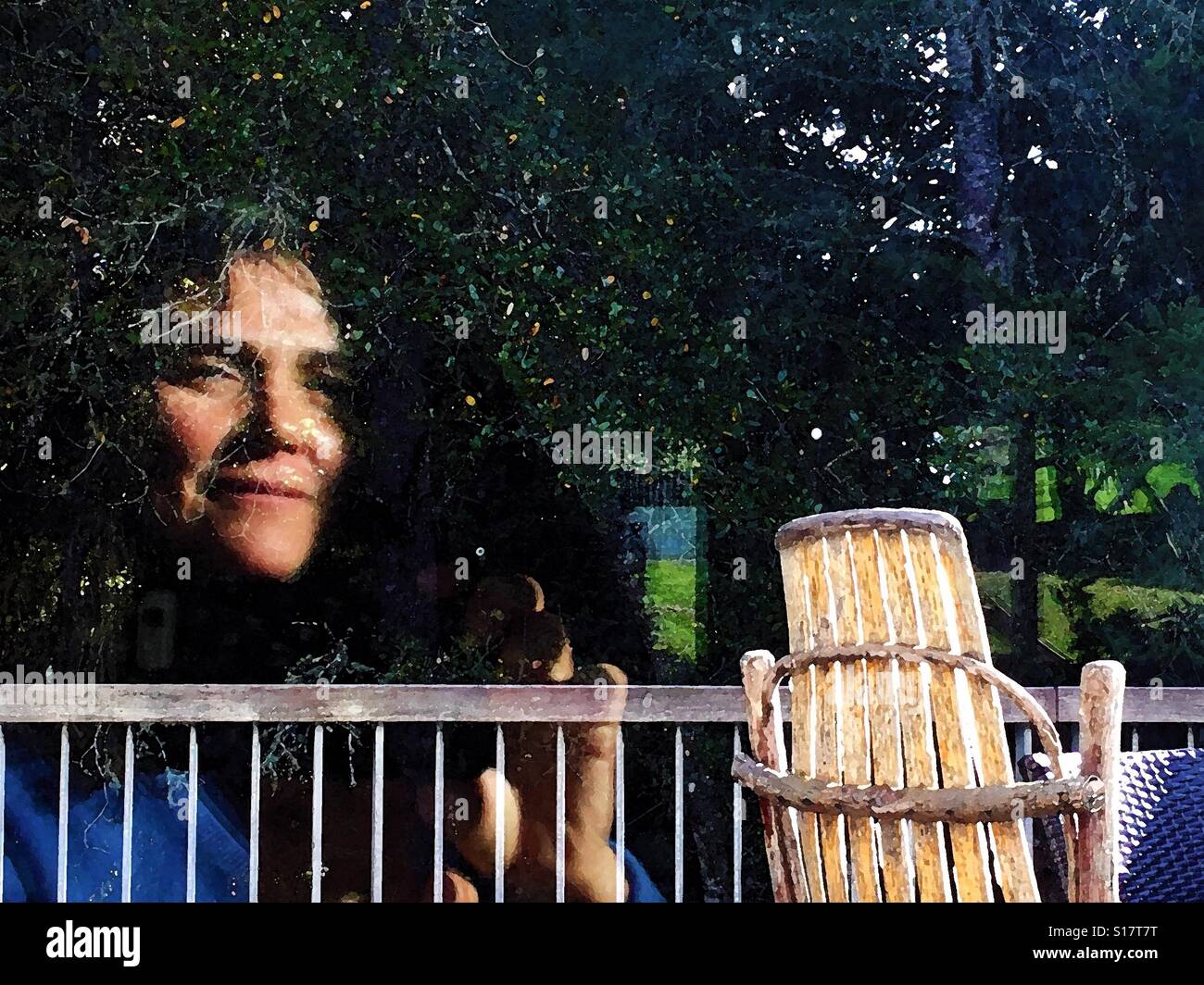 Reflection of woman's face in the trees next to an Andirondack Rocking chair Stock Photo