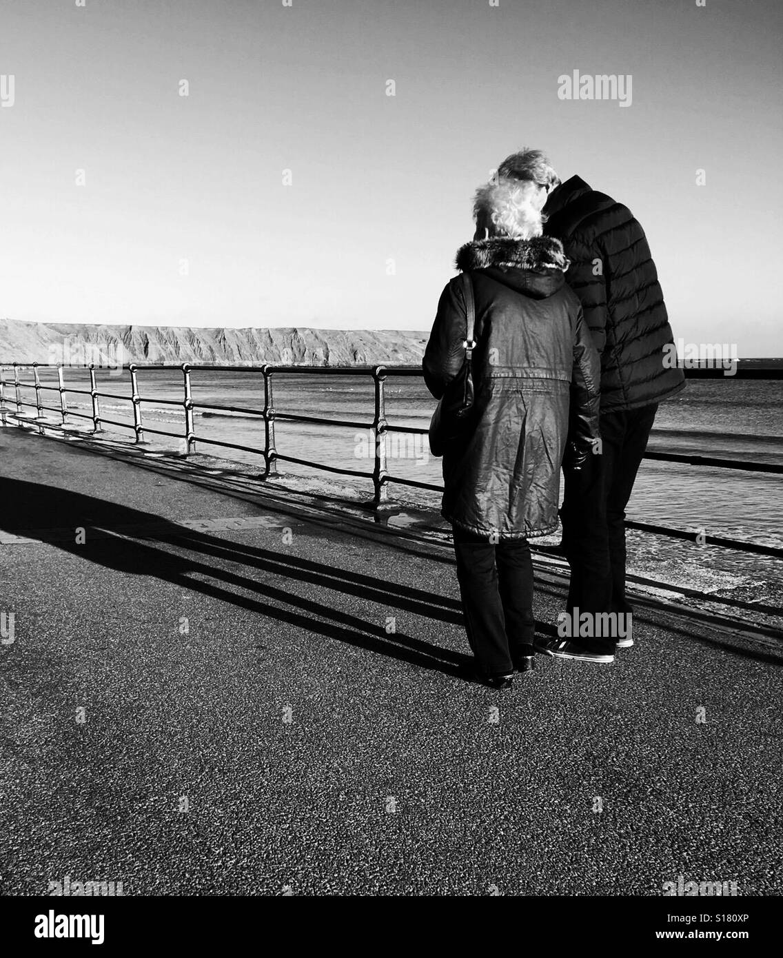 Couple walking along the seafront, pause for a moment - black and white - Smartphone Captured Stock Image