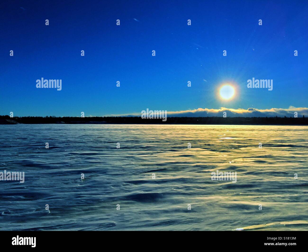 Drifting snow and snow drifts across a frozen lake in December at sunset showing Sunday's and a few stars. Calgary, Alberta, Canada - Smartphone Captured Stock Image