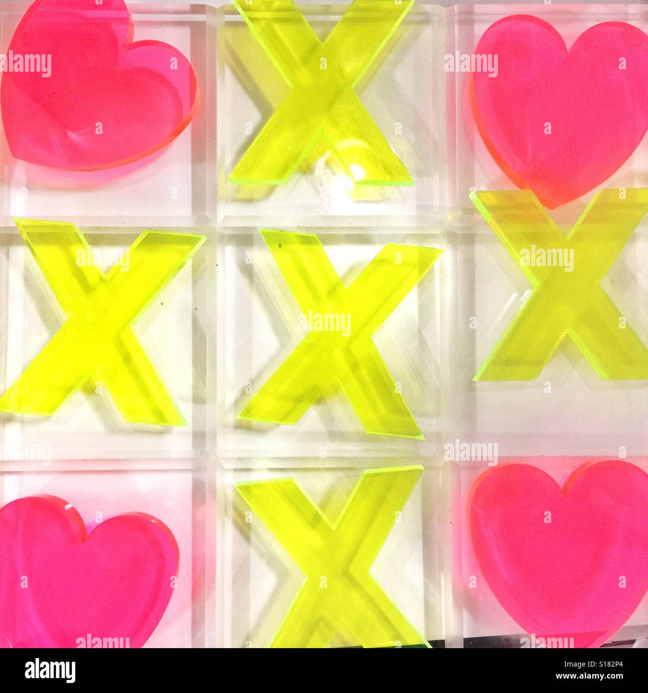 A tic tac toe board of acrylic yellow letter Xs and pink hearts Stock Photo