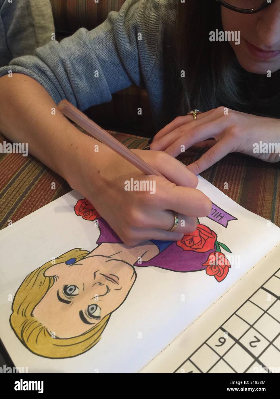 A young woman colors a picture of Hillary Clinton in an adult coloring book Stock Photo