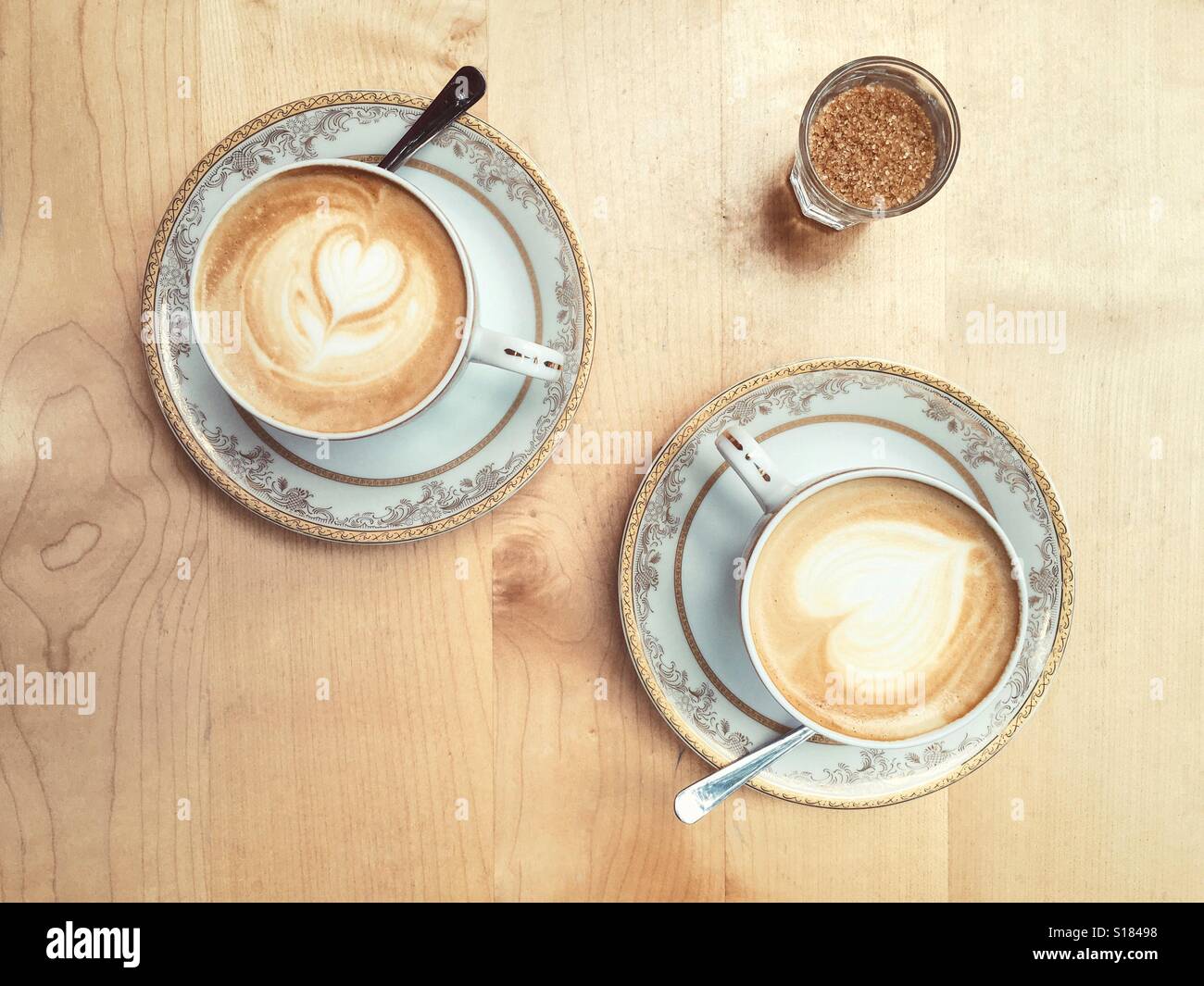 Two coffees on a wooden table and a glass of sugar waiting for a couple to drink them. Seen from above Stock Photo