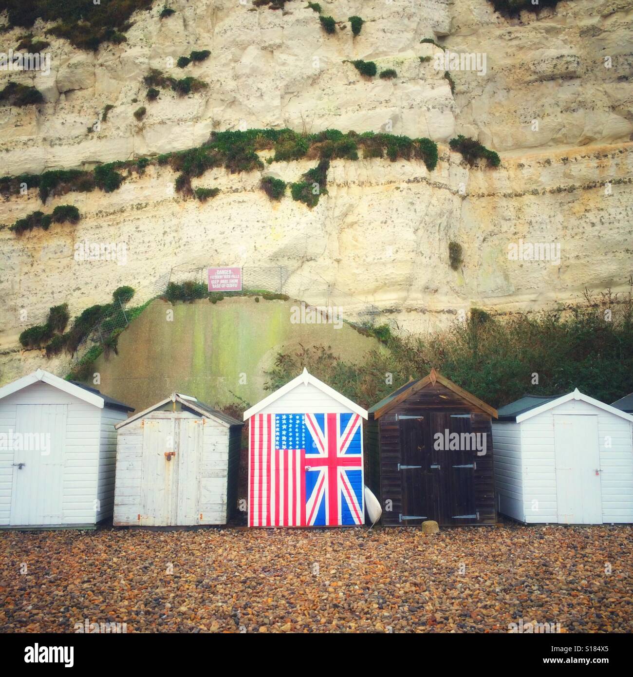 A line of beach huts with one painted in the flags of the UK and USA. Stock Photo