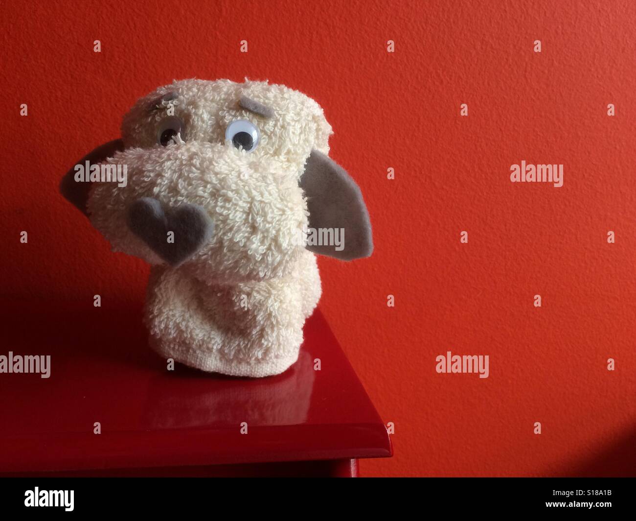 A toy dog made with a hand towel sitting atop a red surface and against a red background. Stock Photo
