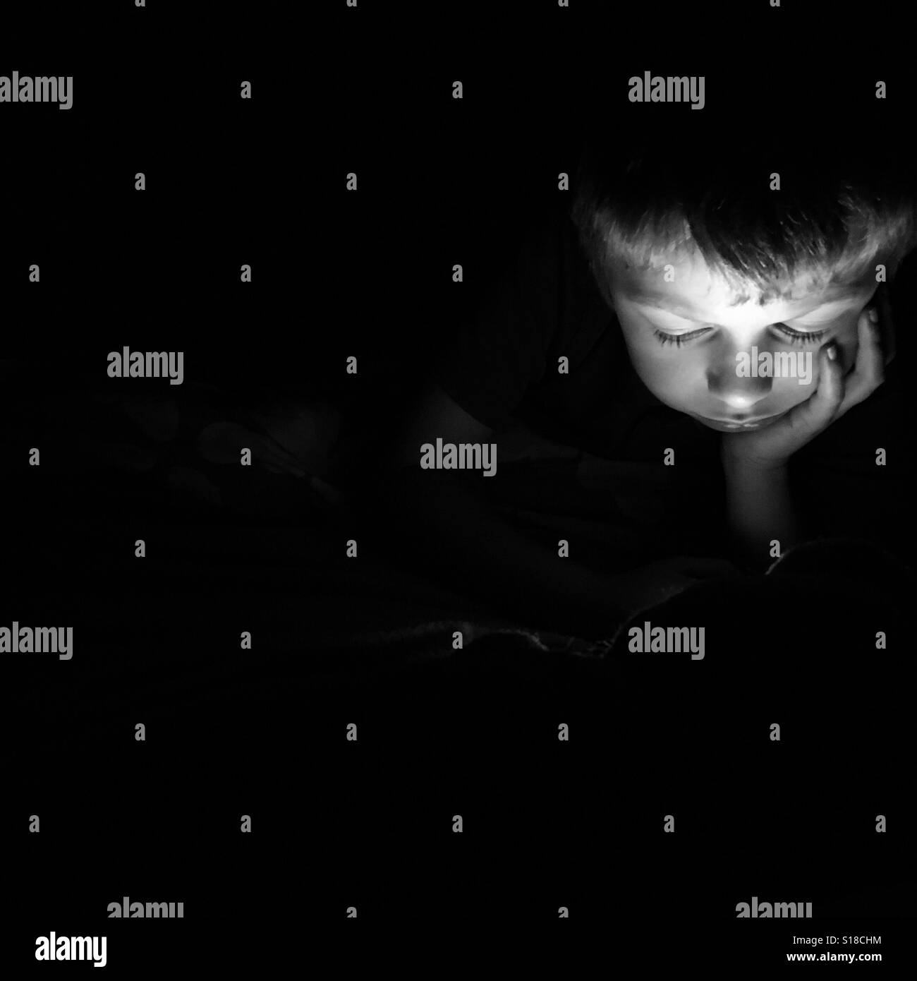 A young boy uses a digital device at night. Stock Photo