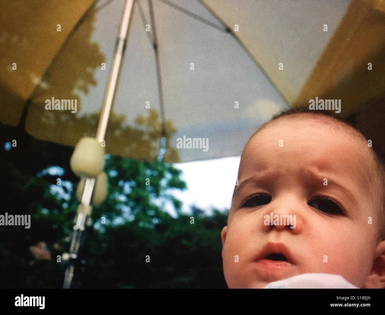 A close up of a baby girl who is sitting under a patio umbrella Stock Photo