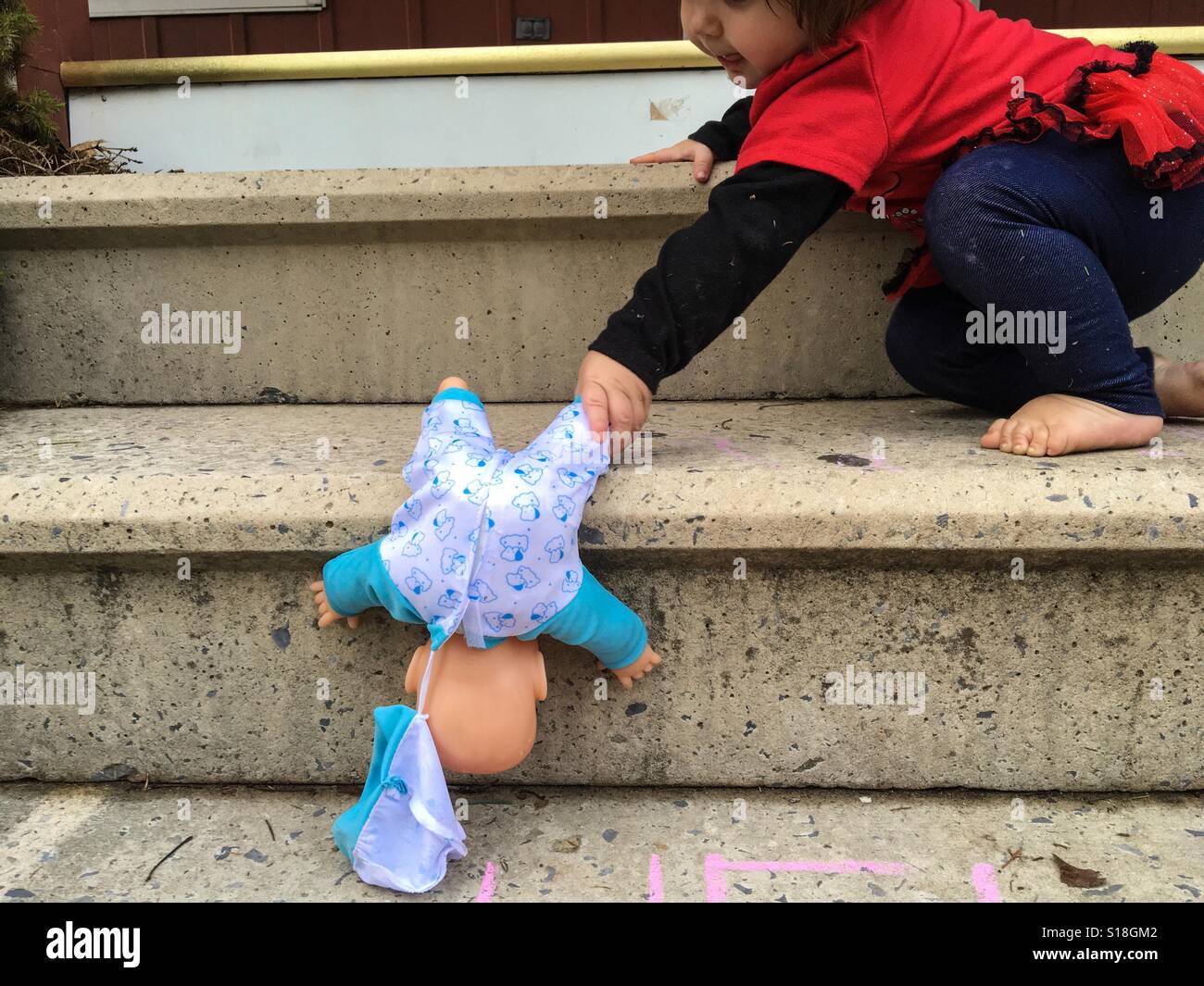 A toddler rescues her doll from falling down the stairs. Stock Photo