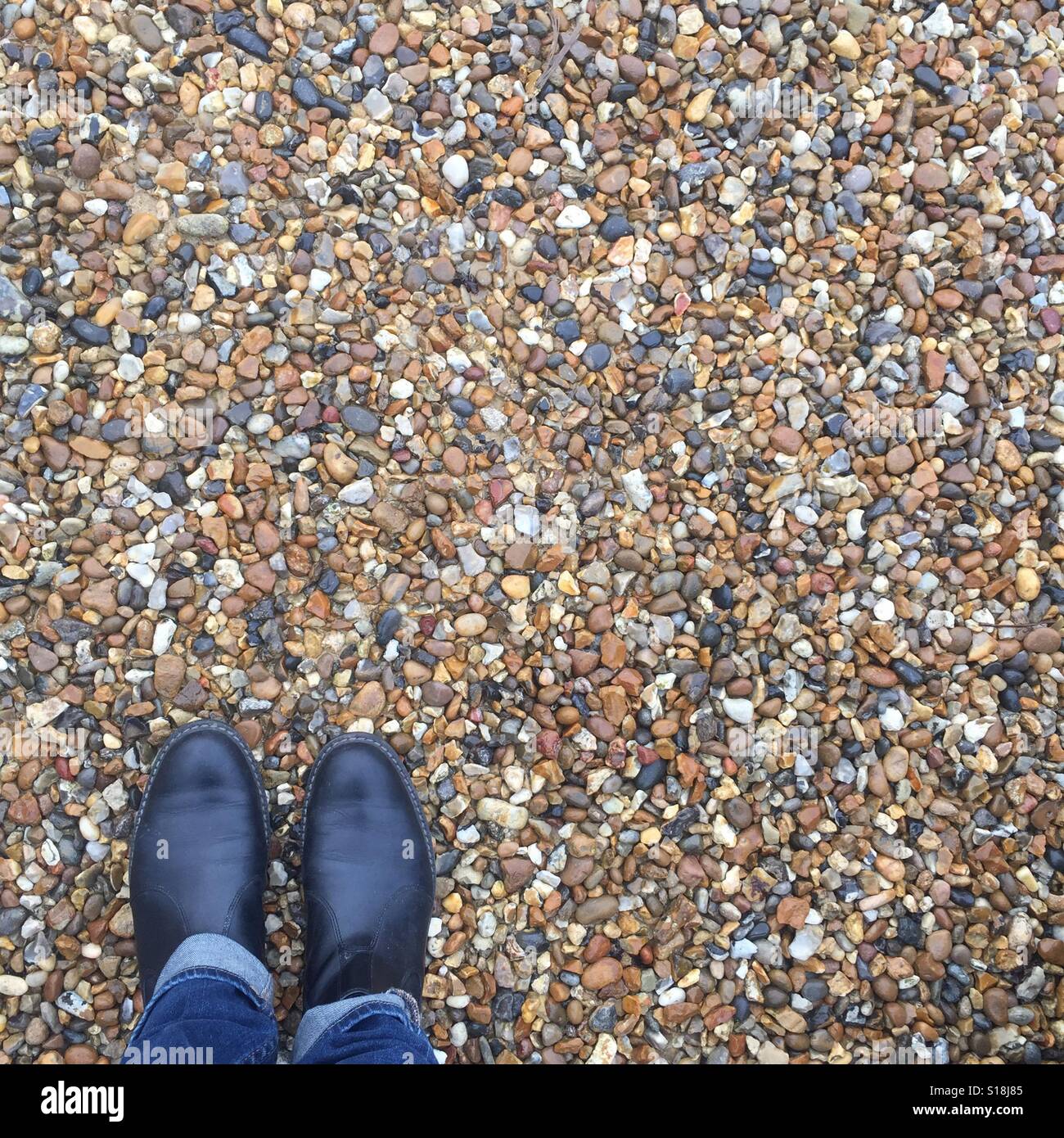 Pebbles background with man standing wearing Chelsea boots. Stock Photo