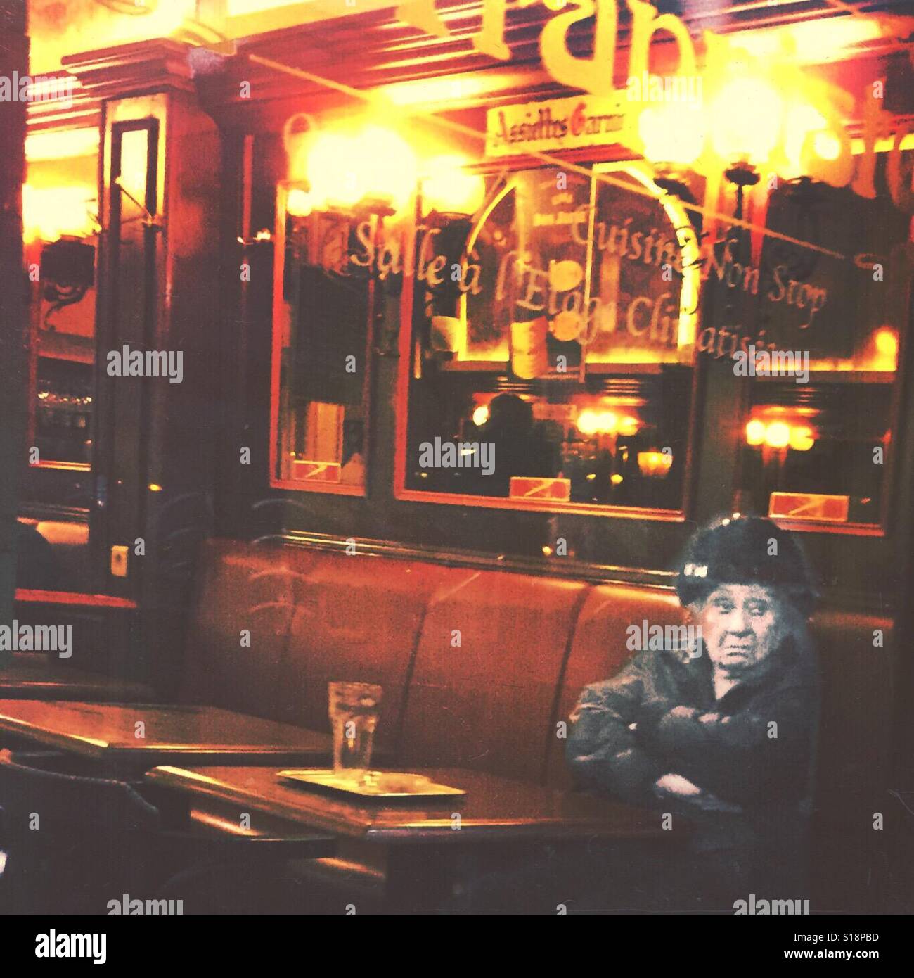 Old woman sitting alone in a pub while looking outside through a window Stock Photo