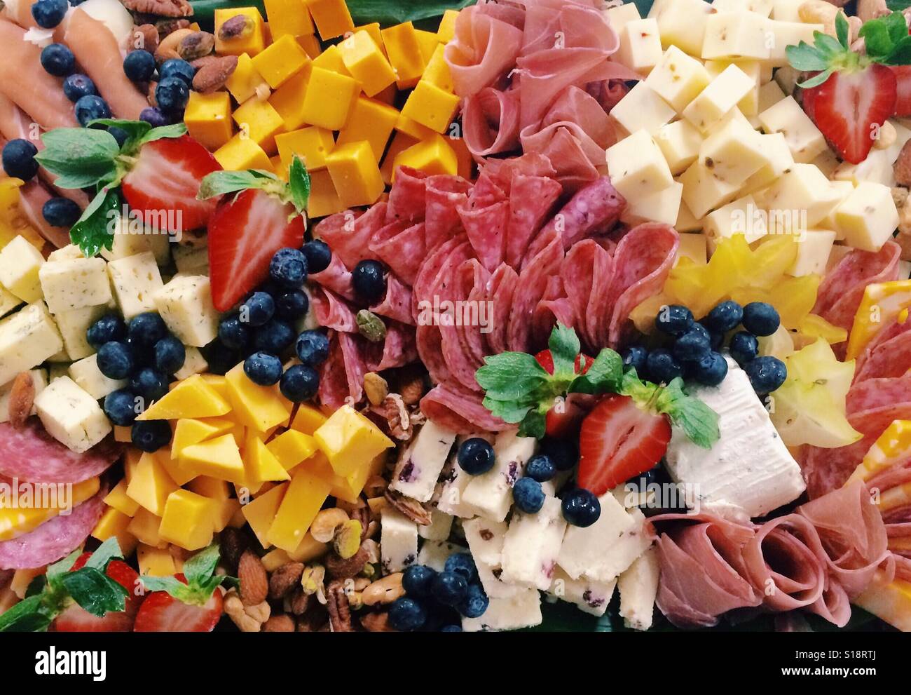 A large catered platter of assorted cheeses, cured meats, berries, and nuts. Stock Photo