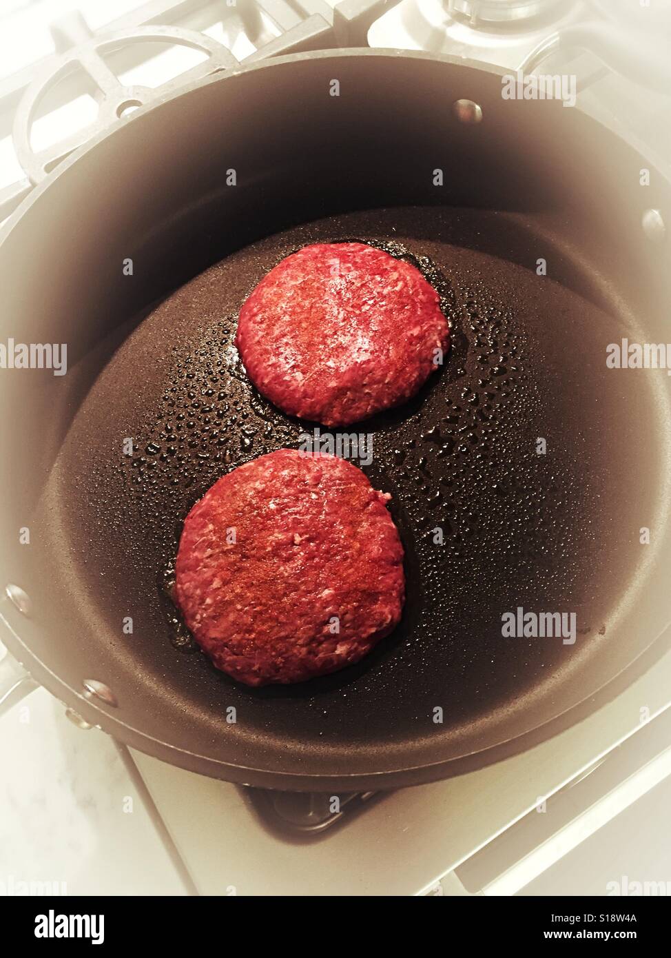 Beef hamburgers frying in a skillet on residential kitchen stove top, USA - Smartphone Captured Stock Image