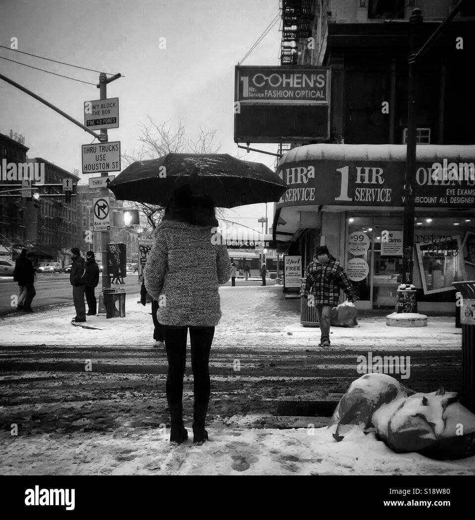 A woman with an umbrella waits to cross a New York City street during a snowstorm. Stock Photo