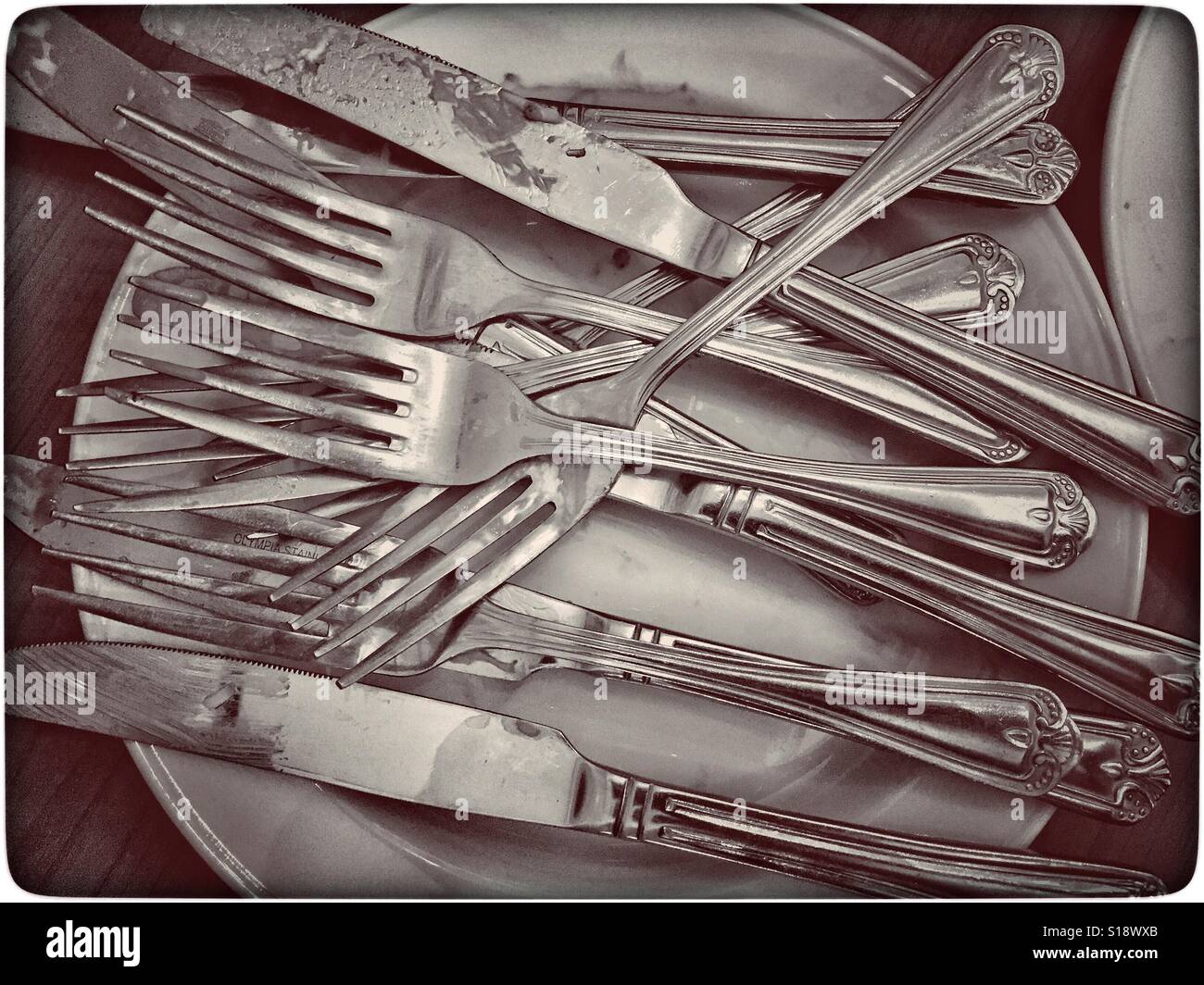 A pile of used knives and forks lie on top of a white plate. The buffet meal is over and the tidying up has started. Photo Credit - © COLIN HOSKINS. - Smartphone Captured Stock Image